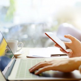 Womens hand typing on a laptop holding a cell phone